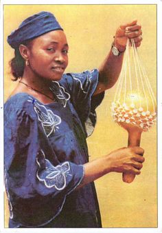 a woman holding a vase with beads on it's neck and wearing a blue dress