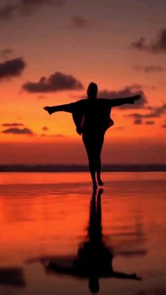 a person standing on the beach with their arms outstretched in front of an orange sky