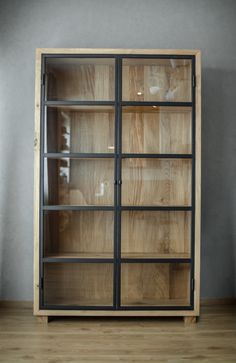 an empty wooden cabinet with glass doors in a room that has wood floors and gray walls