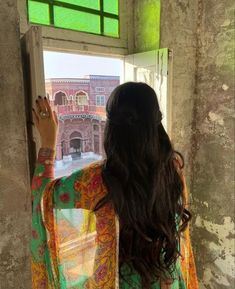 a woman standing in front of a window looking out