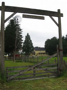 an old wooden gate with a windmill in the background and a farm sign above it