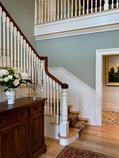 a vase with flowers sitting on top of a wooden table next to a stair case