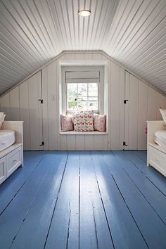 an attic bedroom with white walls and blue flooring is pictured in this image, there are two twin beds on either side of the window sill