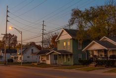 several houses line the street at dusk with power lines in the sky and trees on either side