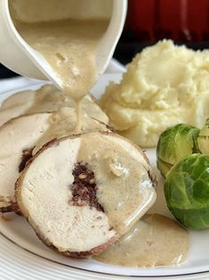 a white plate topped with meat covered in gravy next to mashed potatoes and brussel sprouts