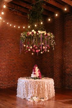 a wedding cake sitting on top of a table with flowers hanging from it's ceiling