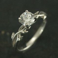 a white gold ring with a diamond in the center and vines on each side, set against a black background