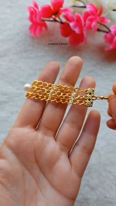 a hand holding a gold chain bracelet with flowers in the background