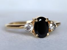 an oval black diamond surrounded by three smaller white diamonds on a yellow gold engagement ring