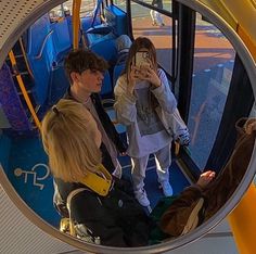 a group of people standing on a bus looking at their cell phones in the mirror