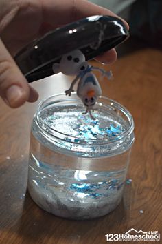 a person is holding a cell phone above a jar filled with water and glitters