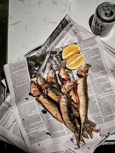 there are fish and lemons on the newspaper next to a can of soda or water