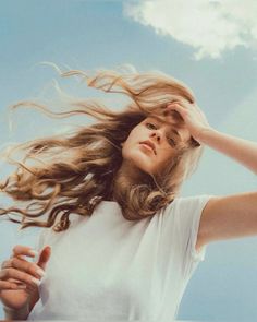 a woman with her hair blowing in the wind and looking up at the blue sky