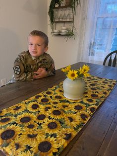 a young boy sitting at a table with sunflowers on the table runner in front of him