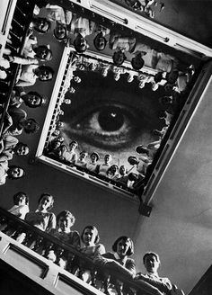 an eye is shown in the middle of a room with many dolls on it and people standing around