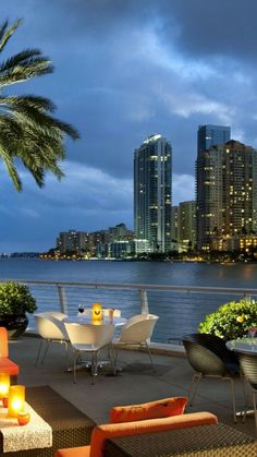 an outdoor dining area overlooking the water and city lights at night, with palm trees in the foreground