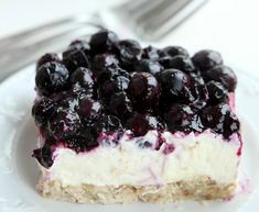 a piece of cheesecake with blueberries and cream filling on a plate next to a fork