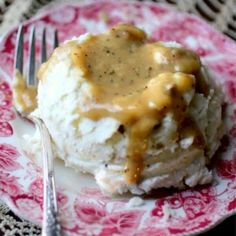 a pink and white plate topped with mashed potatoes covered in gravy next to a fork