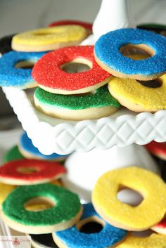 colorful donuts are stacked on top of each other in a white cake stand with red, green, blue, and yellow frosting