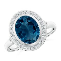 This cocktail ring showcases a mesmerizing oval London blue topaz, bezel set within a halo of pave set round diamonds. It is crafted in 14k white gold with a charming leaf-shaped cutwork on the gallery. Swiss Blue Topaz Ring, Blue Topaz Engagement Ring, Bezel Set Ring, London Blue Topaz Ring, Ring With Diamond, Swiss Blue Topaz, Blue Topaz Ring, London Blue Topaz, London Blue