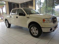 a white pickup truck parked in front of a large glass window with palm trees behind it