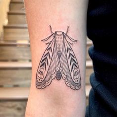 a black and white photo of a moth tattoo on the arm, it looks like an insect