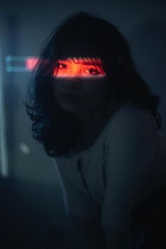 a woman with dark hair and red light on her eyes is staring at the camera