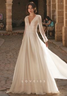 a woman in a wedding dress standing on a cobblestone walkway wearing a long sleeved gown