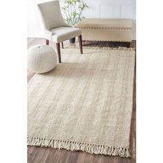 a beige rug with fringes on the floor and a chair next to it in front of a white wall