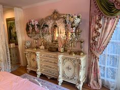 an ornate dresser in the corner of a room with pink walls and drapes on the windowsill