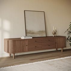 a wooden dresser with two drawers and a mirror on it's sideboard next to a potted plant