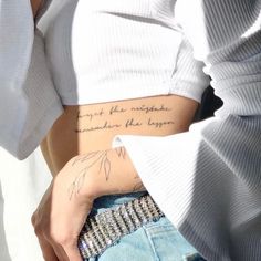 a woman wearing a white shirt and jeans with writing on the side of her stomach