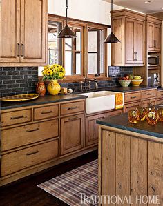 a kitchen with wooden cabinets and black counter tops, an island in the middle has yellow dishes on it