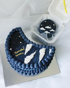 a blue cake with white frosting and stars on it next to a container of cupcakes