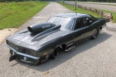 a black muscle car parked on the side of a road next to a wooden fence