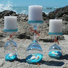 three glass candlesticks with seashells in them on the beach