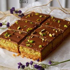 there is a piece of cake with chocolate frosting and nuts on it, next to some purple flowers