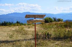 two wooden signs pointing in opposite directions on top of a hill with mountains in the background