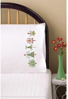 a bed with a green vase and flowers on it next to a white pillow case