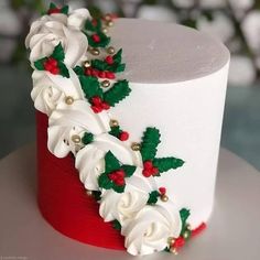 a white and red decorated cake with holly decorations on the top is sitting on a table