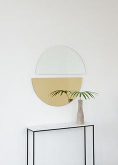 a white table with a plant in it and a round mirror on the wall behind it