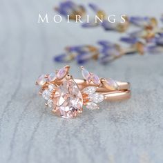 a pink ring with two pear shaped diamonds on it and lavender flowers in the background