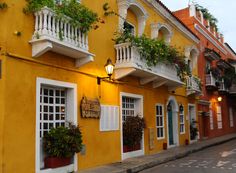 an old yellow building with white balconies and plants growing on it's windows