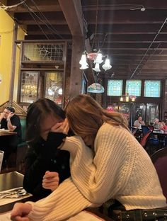 two women are sitting at a table and one is covering her face with her hand