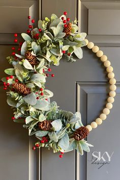 a wreath with pine cones and berries hanging on the front door, decorated with greenery