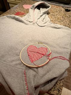 a grey hoodie with a red heart on it and some thread in the middle