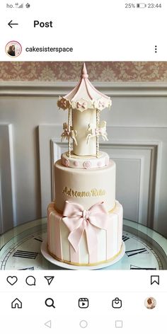 a three tiered cake decorated with pink bows and a carousel on top is sitting on a table in front of a wall