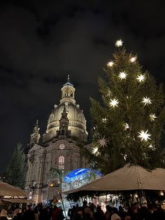 people are standing around in front of a large building with lights on it and a christmas tree