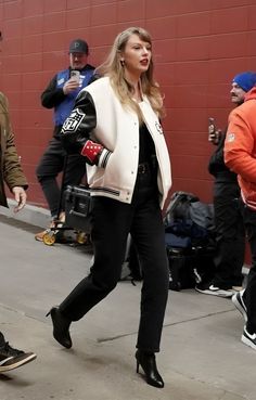 a woman is walking down the street in black pants and a white jacket with patches on it