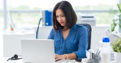 a woman sitting at a desk with a laptop computer in front of her and looking at the screen